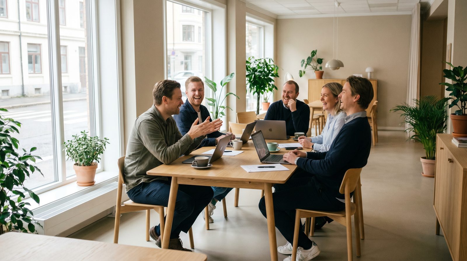 A small team laughing together around a table in a bright Scandinavian office